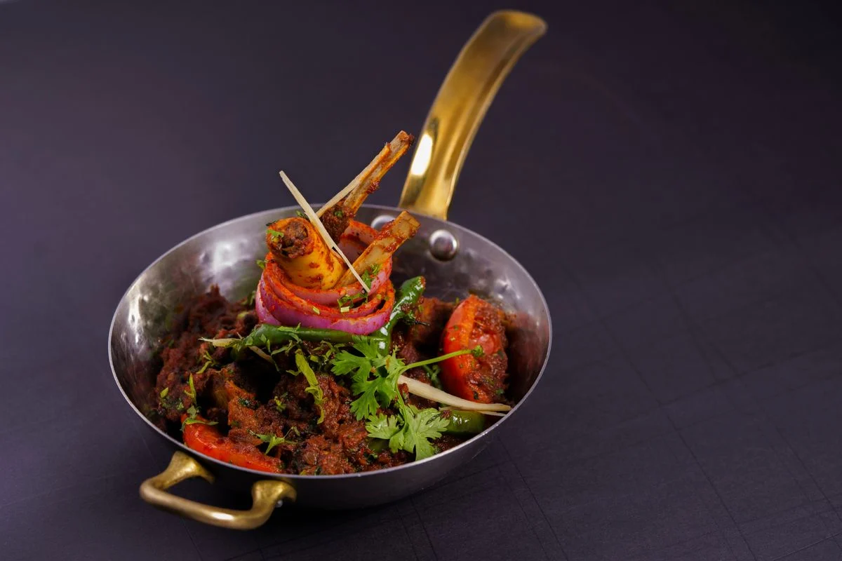 Spicy lamb curry with fresh herbs in a brass pot