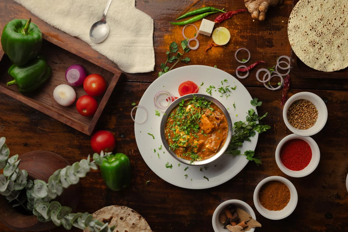 A curry meal surrounded by whole spices and fresh vegetables